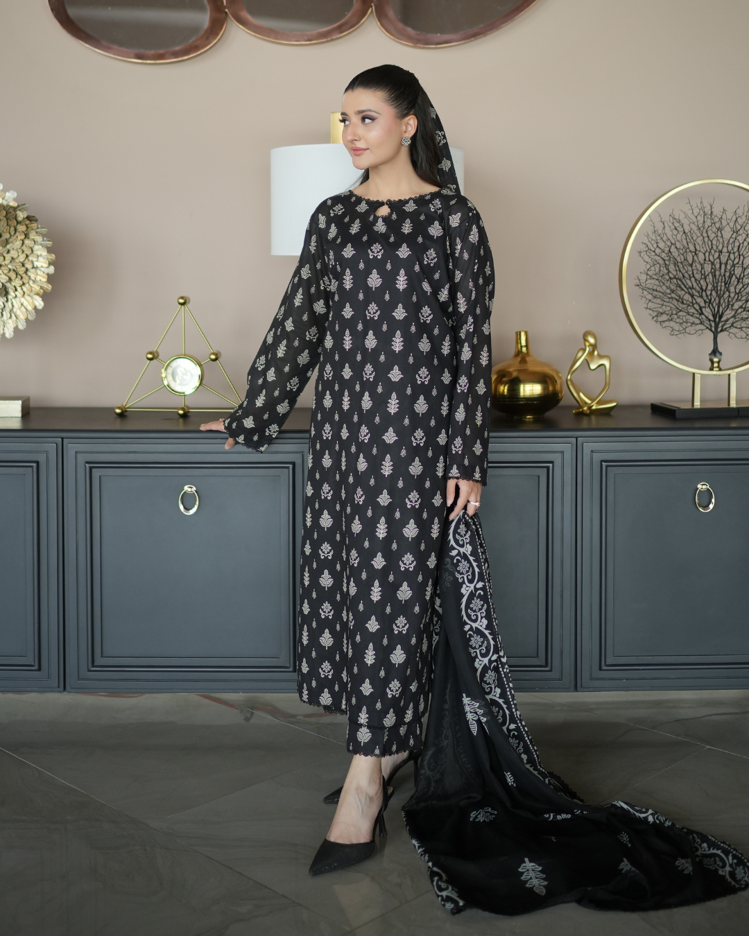 Woman in a black patterned dress standing in a room with decorative elements.