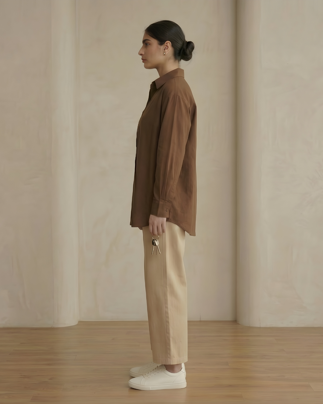 Person wearing a brown shirt and beige pants standing against a plain wall.