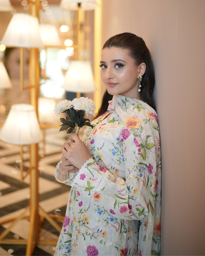 Woman in a floral dress holding flowers indoors with decorative lights in the background
