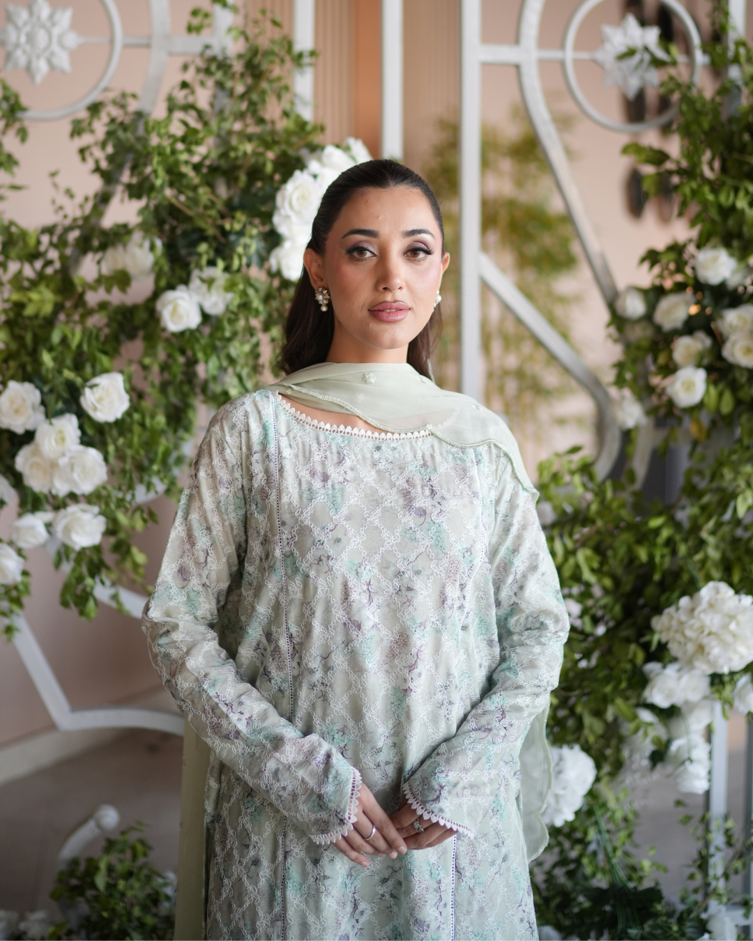 Woman in a light green traditional outfit standing in front of floral decorations - Meryl Wear