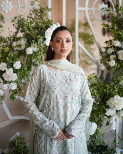 Woman in a light green traditional outfit standing in front of floral decorations - Meryl Wear
