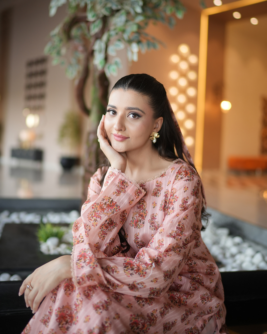 Woman in a floral dress sitting in an indoor setting with decorative elements.
