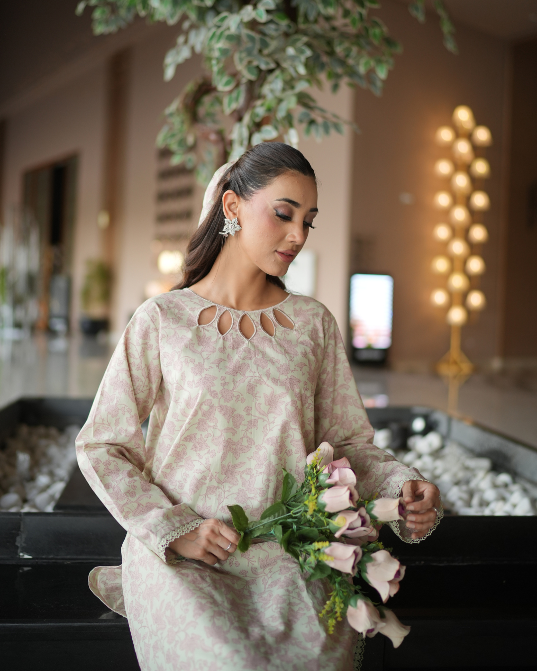Woman in a light-colored dress holding flowers in an indoor setting with decorative elements.