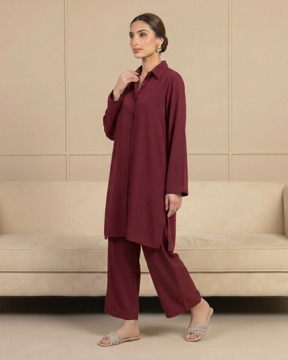 Woman wearing a burgundy outfit standing in front of a beige wall.