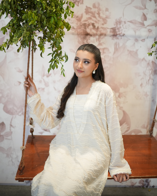 Woman in a white outfit sitting on a wooden swing with a floral background