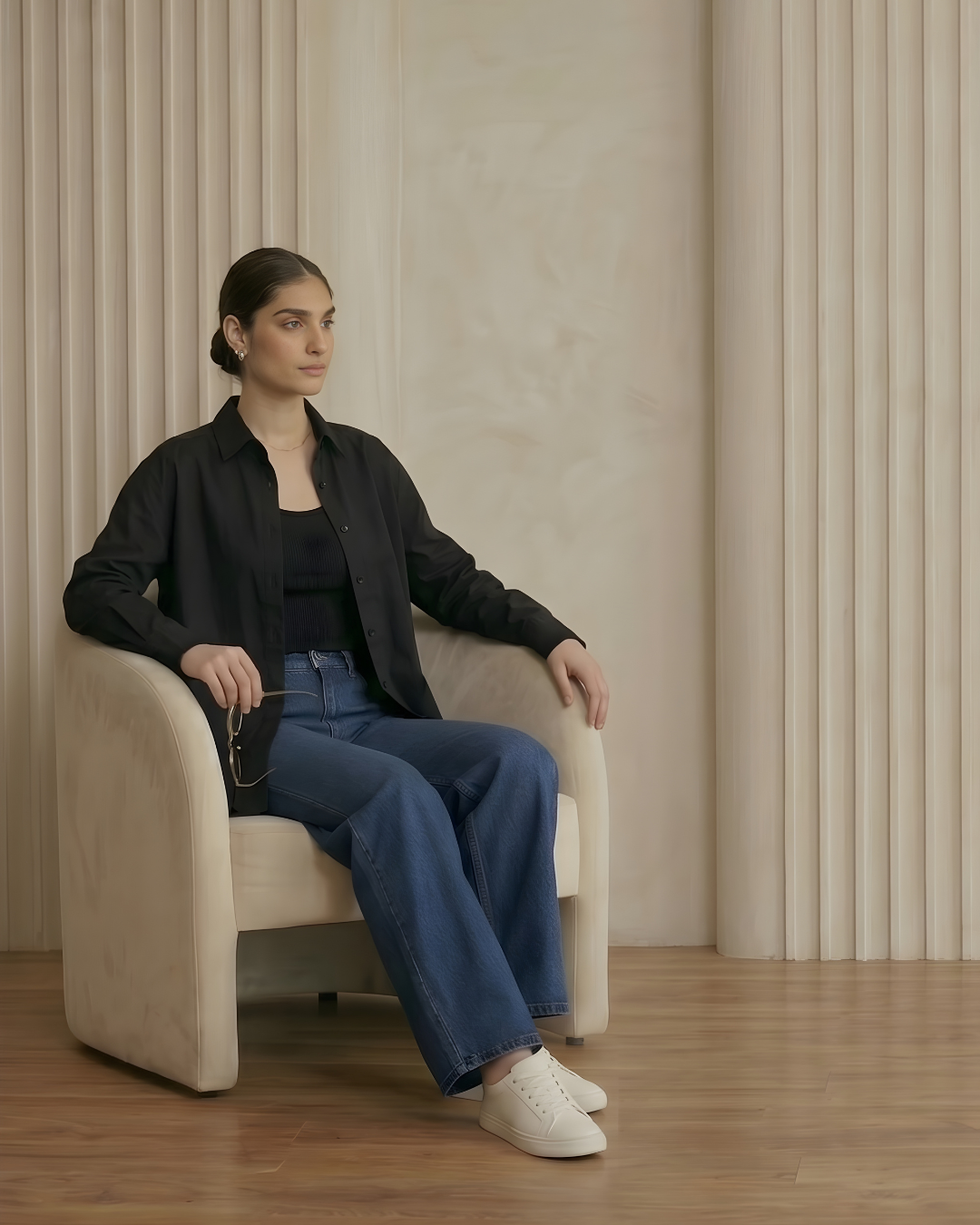 Woman sitting on a beige chair in a room with beige walls and wooden floor.