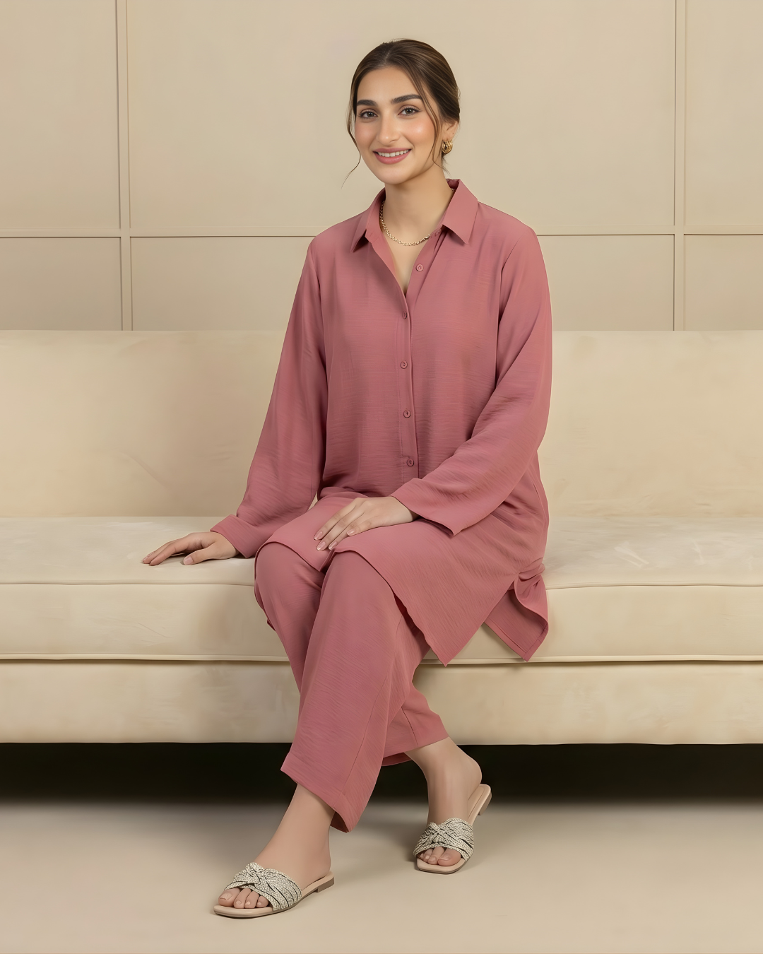 Woman in a pink outfit sitting on a beige couch against a neutral wall wearing a dress by Meryl Wear